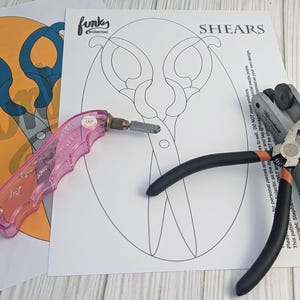 May include: A close-up of a glass cutting project with a pair of shears pattern. The image shows a pink glass cutter, a pair of pliers, and a metal tool for cutting glass. The text on the paper reads "SHEARS" and "funky creations".