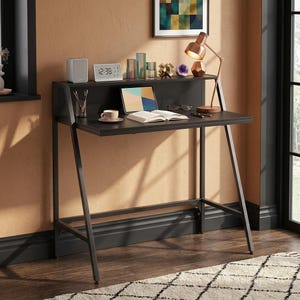 May include: A black metal desk with an A-frame design, featuring a raised upper shelf for storage. The desk surface holds a tablet, an open book, a coffee cup, a pen holder, and a copper-toned desk lamp. A digital clock sits on the top shelf.