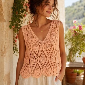 May include: A sleeveless peach-colored crochet top featuring an intricate pineapple stitch pattern throughout the body, a deep V-neckline, and a scalloped hemline. The garment is constructed with a delicate openwork design and a lightweight texture.