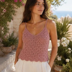 Op de afbeelding: Een oudroze gehaakte tanktop met een delicaat geschulpt schelppatroon, een V-hals en dunne spaghettibandjes. Het kledingstuk wordt gecombineerd met een witte broek, wat zorgt voor een luchtige uitstraling met een gestructureerd opengewerkt ontwerp.