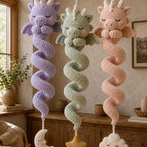 Peut inclure: Trois décorations suspendues en crochet représentant des dragons de couleur lavande, vert sauge et pêche. Chaque dragon a les yeux fermés, de petites ailes et une longue queue en spirale terminée par une lune crème, une étoile jaune ou un nuage blanc.