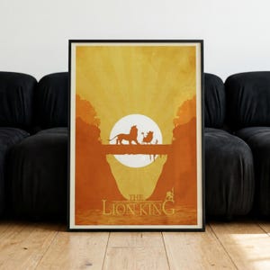 May include: A rectangular poster featuring a stylised orange and yellow sunset scene with silhouettes of a lion, a warthog, and a meerkat walking on a log. The text THE LION KING is printed in a bold, serif font at the bottom of the artwork.