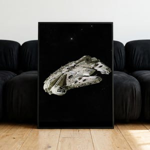 Op de afbeelding: Een ingelijste rechthoekige wandkunstprint met het Millennium Falcon ruimteschip dat door de diepe ruimte vliegt. Het ruimtevaartuig is afgebeeld in grijstinten en wit tegen een diepzwarte achtergrond vol verspreide sterren.