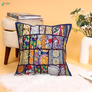 Pode incluir: Uma almofada quadrada com um design de patchwork feito de vários tecidos bordados em cores vibrantes, incluindo azul, dourado, vermelho e verde. A almofada é construída a partir de vários painéis retangulares com padrões florais e geométricos intrincados.