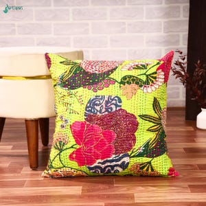 May include: A square throw pillow featuring a vibrant lime green background with a multi-colored floral pattern. The design includes large pink, dark blue, and white flowers with intricate stitching details throughout the fabric surface.