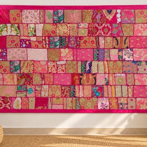 Puede incluir: Un tapiz rectangular para colgar en la pared compuesto por numerosos cuadrados de tela de patchwork en varios tonos de rosa, magenta y dorado. El tejido presenta intrincados patrones bordados, hilos metálicos y motivos florales.