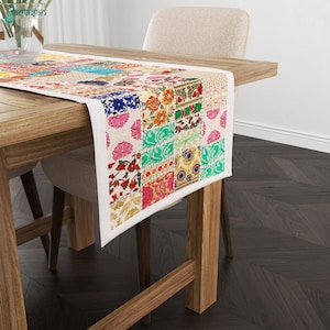Könnte beinhalten: Ein rechteckiger Tischläufer mit einem Patchwork-Design aus verschiedenen Blumen- und geometrischen Mustern in leuchtenden Farben wie Rot, Orange, Blau, Grün und Pink auf cremefarbenem Hintergrund, drapiert über einem Holztisch.