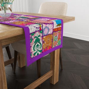 Könnte beinhalten: Ein rechteckiger Tischläufer mit einem lebendigen Patchwork-Design, das verschiedene florale und geometrische Muster in den Farben Violett, Pink, Grün, Orange und Weiß aufweist. Der Läufer ist an den Rändern mit einer violetten Stoffborte eingefasst.