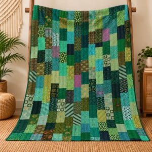 May include: A rectangular patchwork quilt featuring a variety of green, teal, and blue fabric rectangles stitched together. The quilt displays diverse patterns including geometric shapes, floral motifs, and solid colours with visible running stitch details.