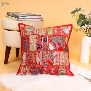 May include: A square throw pillow featuring a vibrant red patchwork design with intricate gold embroidery, sequins, and multi-colored floral and paisley patterns. The fabric is composed of various stitched panels, creating a textured surface.