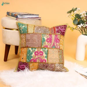 Könnte beinhalten: Ein quadratisches Zierkissen mit einem Patchwork-Design aus verschiedenen bestickten Stoffen in Rosa-, Grün-, Gold- und Beigetönen. Das Kissen ist mit komplexen Blumenmustern, Pailletten und metallischen Fadenstickereien auf der Oberfläche verziert.