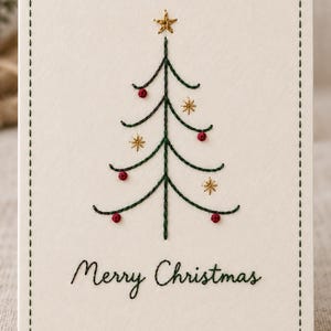Puede incluir: Una tarjeta de felicitación de color crema con un diseño bordado a mano de un árbol de Navidad verde, estrellas doradas y pequeños adornos circulares rojos. El texto Merry Christmas está bordado en hilo verde y un borde cosido enmarca la tarjeta.