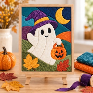 May include: A framed fabric wall art piece featuring a white ghost wearing a purple witch hat with a yellow band. The ghost holds an orange jack-o'-lantern bucket against a background of rolling hills, a yellow crescent moon, and autumn leaves.