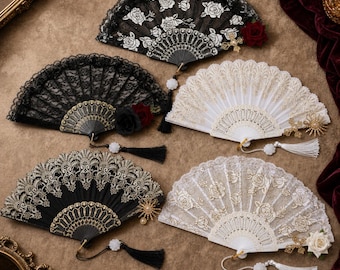 May include: Five folding hand fans featuring intricate lace and fabric designs. Three fans are black with gold or white floral patterns and accents, while two are white with gold floral embroidery. Each fan includes a tassel and decorative charm.