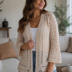 Könnte beinhalten: Eine beigefarbene, vorne offene Strickjacke mit einem komplexen Häkelmuster mit floralen Motiven, langen Ärmeln und einem geraden Saum. Das Kleidungsstück ist aus hellem Garn gefertigt und zeigt ein detailliertes, strukturiertes Strickmuster.