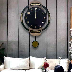 Puede incluir: Un reloj de pared con una esfera circular negra y números dorados del 1 al 12, enmarcado en un anillo negro con detalles en tono madera. El reloj incluye un péndulo con un peso circular dorado que cuelga de la parte inferior.
