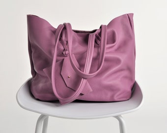 Può includere: Una grande borsa tote in morbida pelle viola con due manici lunghi. La borsa è appoggiata su una sedia bianca.