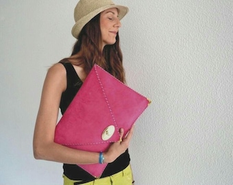 Può includere: Una pochette rosa acceso a forma di busta con chiusura dorata e cuciture bianche. La borsa è tenuta contro un muro bianco. Un accessorio elegante.