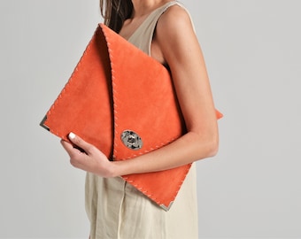 Può includere: Pochette in camoscio arancione con una forma triangolare unica. Presenta cuciture a vista, angoli in metallo e una chiusura decorativa argentata. Un accessorio elegante.