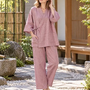 Op de afbeelding: Een tweedelige loungewear-set in oudroze, bestaande uit een wikkel-top met driekwartmouwen, een striksluiting aan de zijkant en een opgestikte zak, gecombineerd met een bijpassende, losvallende broek met rechte pijpen van gestructureerde stof.