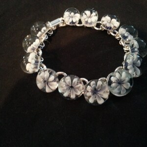 May include: A silver chain bracelet with white and blue glass flower beads.