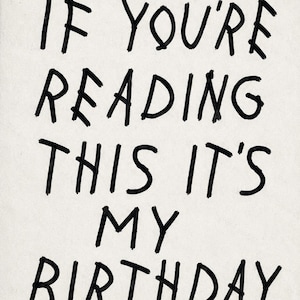 Op de afbeelding: Een rechthoekige witte kaart met de zwarte handgeschreven tekst IF YOU'RE READING THIS IT'S MY BIRTHDAY. De letters zijn in een informele, onregelmatige stijl die lijkt op een stift, gecentreerd op een effen, lichte achtergrond.