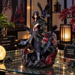 Può includere: Una dettagliata statuetta di un personaggio anime con capelli neri che indossa un lungo cappotto nero con motivi a nuvole rosse. La figura poggia su una base di fiamme nere e rosse vorticose, circondata da diversi corvi neri con riflessi blu.