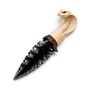 May include: A dagger featuring a sharp, black, obsidian-like blade with serrated edges. The handle is sculpted into the shape of a cobra head with cream-coloured scales and red eyes, connected to the blade by an ornate, dark bronze-coloured metal collar.