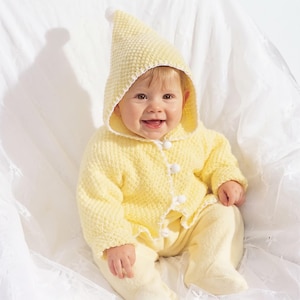 Könnte beinhalten: Eine hellgelbe Kapuzenjacke mit strukturiertem Strickmuster, einer spitzen Kapuze mit einem kleinen weißen Bommel an der Spitze, weißem Wellensaum an den Kanten und drei weißen, kugelförmigen Knöpfen in der vorderen Mitte des Kleidungsstücks.