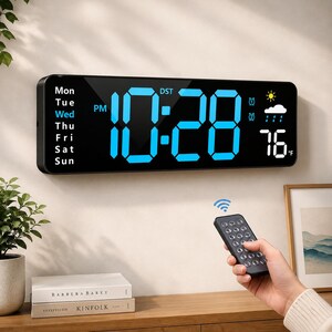 May include: A rectangular black digital wall clock with a large blue LED display showing the time 10:28, the day of the week, and weather icons. The clock displays 76 degrees Fahrenheit and includes a remote control for wireless operation.