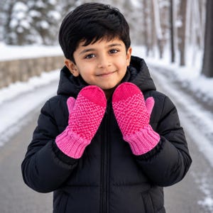 Könnte beinhalten: Ein Paar leuchtend pinke Strickfäustlinge mit einem strukturierten, zweifarbigen geometrischen Muster auf dem Hauptteil und einem einfarbigen, gerippten Bündchen in Pink. Die Fäustlinge werden über den Händen getragen und zeigen ein kräftiges Pink.