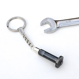 May include: A silver wrench and a black and silver keychain with a bolt-shaped charm are displayed on a white background. The wrench is marked with "1/2". The keychain has a chain and a ring.