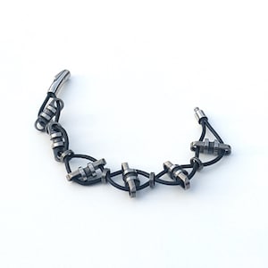 Könnte beinhalten: Ein schwarzes Lederarmband mit silbernen Metallakzenten. Das Armband besteht aus einer Reihe von miteinander verbundenen Metallteilen und Lederriemen.