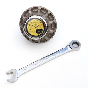 Könnte beinhalten: Eine Uhr mit gelbem Zifferblatt und schwarzen Ziffern ist in einem grauen, kreisförmigen Gehäuse untergebracht. Ein silberner Schraubenschlüssel mit dem Text "Halfords Professional" und "1/2" ist darunter positioniert.