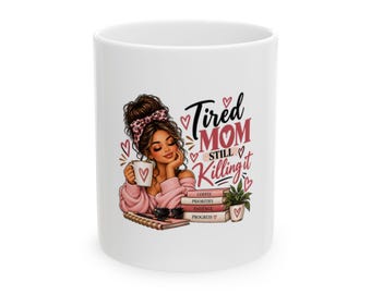 Puede incluir: Una taza de cerámica blanca con una ilustración gráfica de una persona con un moño y una diadema de leopardo sosteniendo una taza. El texto dice "Tired MOM STILL Killing it" junto a una pila de libros etiquetados como Coffee, Priorities, Patience, Progress.