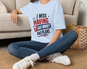 Puede incluir: Una camiseta de manga corta de color azul claro con el texto I MISS HAVING GAS MONEY AND PLANS en letras rojas, blancas y azules. El gráfico incluye un pequeño icono de surtidor de gasolina rojo y detalles de pinceladas azules.
