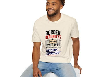 Puede incluir: Una camiseta de manga corta de color crema con un gráfico de una valla de alambre y un cartel que dice WELCOME. El texto superior dice BORDER SECURITY? y el texto inferior dice WE THOUGHT YOU SAID WELCOME COMMITTEE.