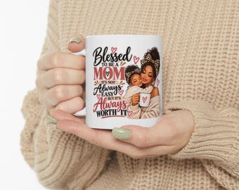 Puede incluir: Una taza de cerámica blanca con una ilustración gráfica de un padre y un hijo con diademas de estampado de leopardo. El texto dice: Blessed to be a MOM it's not always easy but it's always worth it. Pequeños corazones rojos rodean el texto.