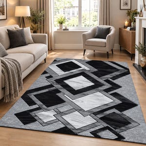 May include: A rectangular area rug featuring a geometric pattern of overlapping squares in shades of black, white, and grey. The design consists of solid black squares and textured grey and white squares arranged in a layered, cascading composition.