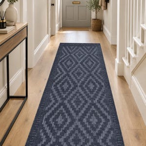 May include: A long, rectangular runner rug featuring a dark navy blue and charcoal grey geometric diamond pattern. The rug has a flat-woven texture with a repeating motif of nested diamonds and a bordered edge, extending across the floor.