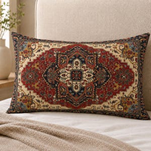 May include: A rectangular throw pillow featuring a detailed, intricate pattern in shades of deep red, navy blue, cream, and gold. The design displays a central medallion surrounded by geometric borders and floral motifs, mimicking the style of a rug.