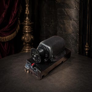 Könnte beinhalten: Ein schwarzer Nähmaschinenmotor aus Metall mit einem runden Riemenrad an einer Seite und einem rechteckigen Sockel. Der Motor hat eine glatte, dunkle Oberfläche mit einem kleinen roten Akzent am vorderen Schalter und sichtbaren Metallteilen.