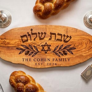 May include: An oval olive wood serving board featuring a laser-engraved Star of David, olive branches, and Hebrew text. The board is personalized with the text THE COHEN FAMILY and EST. 2026, centered on the natural wood grain surface.