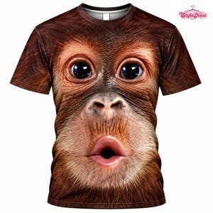 May include: A short-sleeved t-shirt featuring a high-definition, full-front graphic print of an orangutan face with large dark eyes and pursed lips. The fur texture is rendered in shades of brown and tan, covering the entire front of the garment.