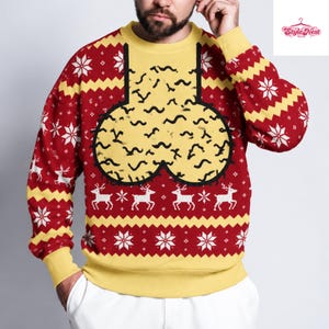 Peut inclure: Un pull à col rond et manches longues avec un motif tricoté rouge et jaune orné de flocons de neige et de rennes blancs. Le centre présente un grand graphique jaune arrondi avec des lignes noires ondulées, souligné de noir.