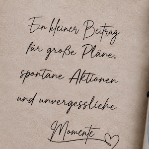 May include: A light brown card with black cursive text that reads: Ein kleiner Beitrag f&uuml;r gro&szlig;e Pl&auml;ne, spontane Aktionen und unvergessliche Momente, accompanied by a heart symbol. Next to it is a glass tube with a cork stopper containing a rolled banknote.
