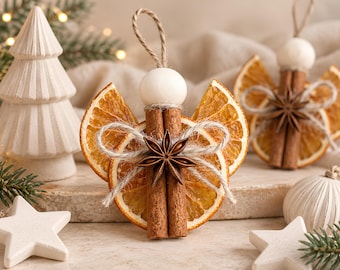 May include: Two angel ornaments crafted from dried orange slices for wings, cinnamon sticks for bodies, and a wooden bead for a head. A star anise is attached to the centre with twine, and a jute loop is at the top for hanging.