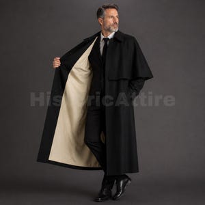 Könnte beinhalten: Ein langer schwarzer Mantel mit Cape-Überwurf und kontrastierendem beigefarbenem Innenfutter. Der Mantel verfügt über einen strukturierten Kragen, lange Ärmel und eine bodenlange Silhouette. Er wird über einem schwarzen Anzug getragen.