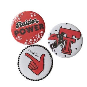 May include: Three circular pin-back buttons. One red button features white pearls and the text Raider POWER. One white button displays a black and red horse and rider logo with a large red T. One white button features a red hand and Wreck'Em text.