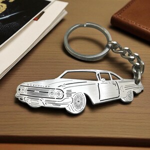 Può includere: Un portachiavi in metallo color argento con la sagoma tagliata al laser di un'auto Chevrolet d'epoca. Il design presenta incisioni dettagliate della griglia anteriore, dei fari, delle ruote e della scritta Chevrolet sul cofano, con anello.